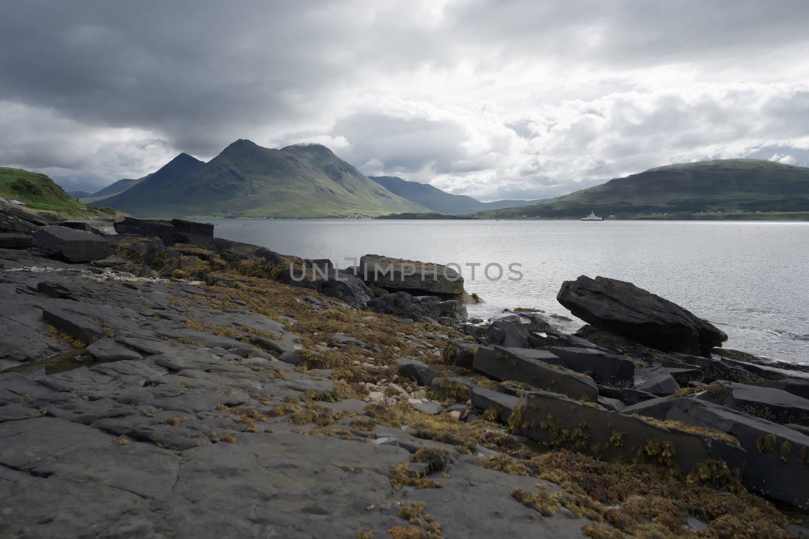 Coastal landscape from the isle of raasay looking towards the isle of skye. Ferry travels the sea under the peak of Glamaig which is cloud topped.