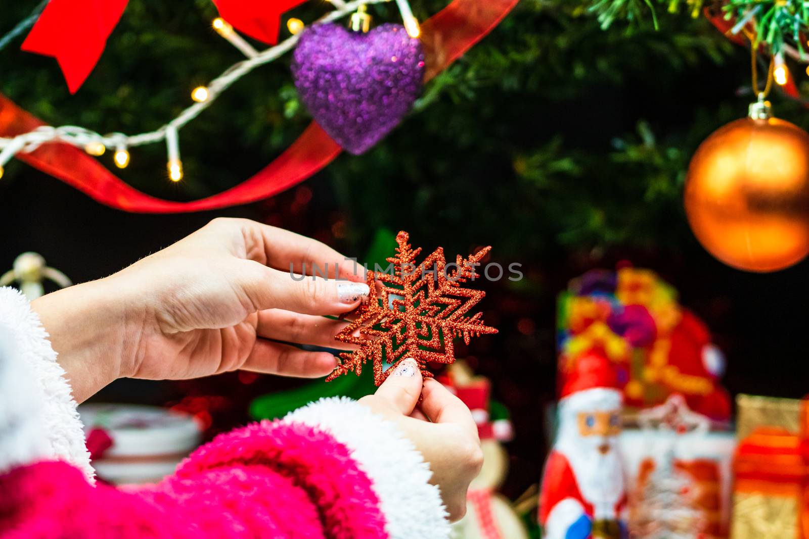 Hands holding Christmas ornament in front of Christmas tree. Decorating fir branches with Christmas decorations.