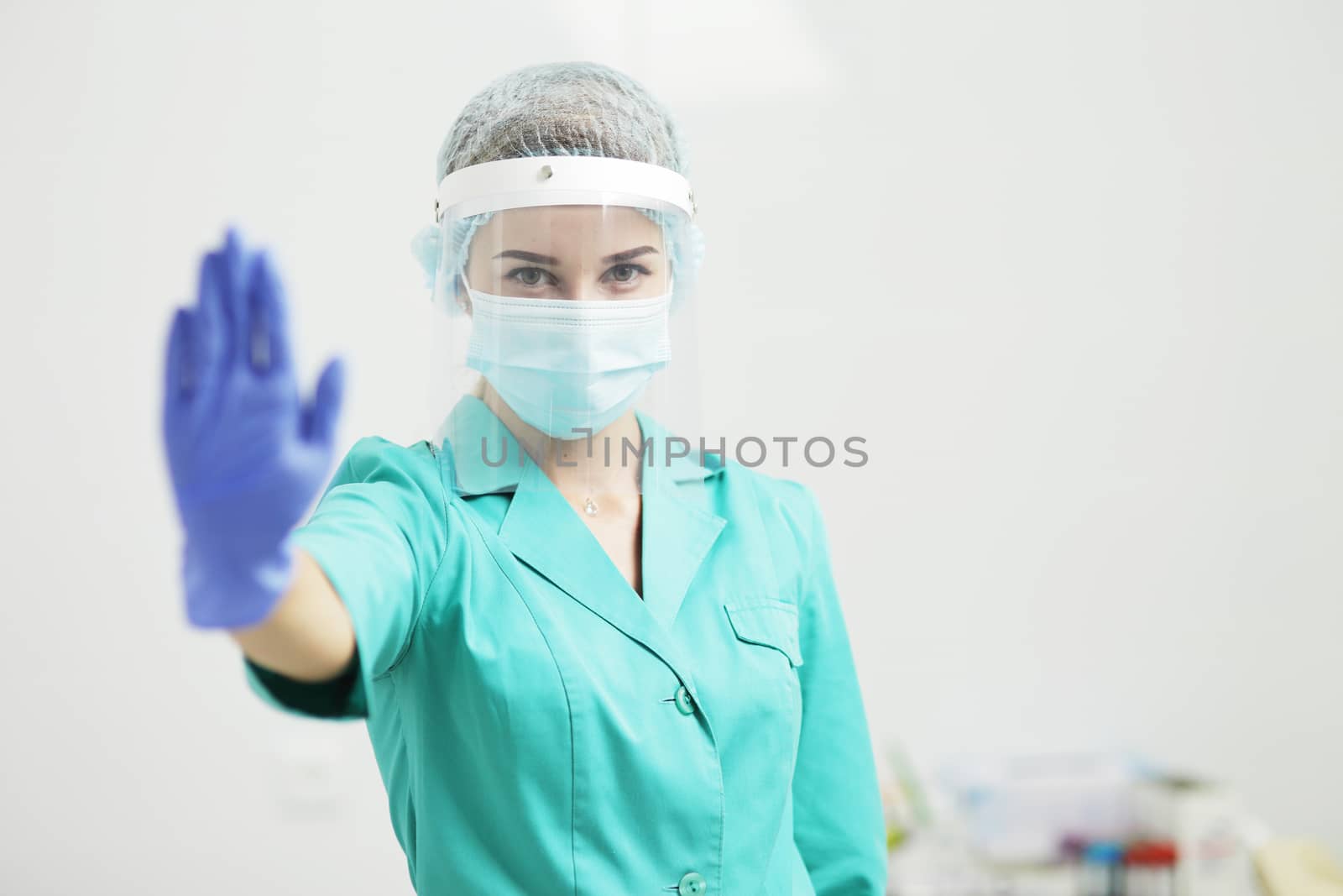 A Female doctor or nurse in uniform, medical mask, protective shield, and gloves shows stop gesture with hand. Coronavirus Covid-19. Girl, woman.