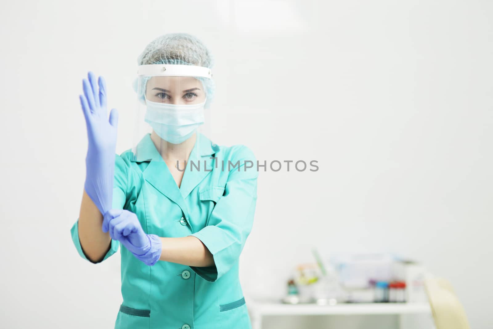 Female doctor or nurse in uniform, medical mask, face shield puts on gloves. Coronavirus COVID-19. Girl, woman.