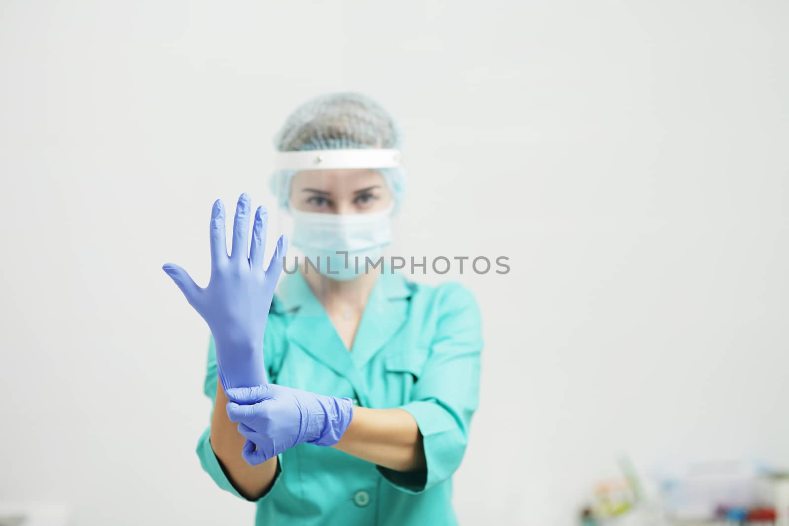 Female doctor or nurse in uniform, medical mask, face shield puts on gloves. Coronavirus COVID-19. Girl, woman.