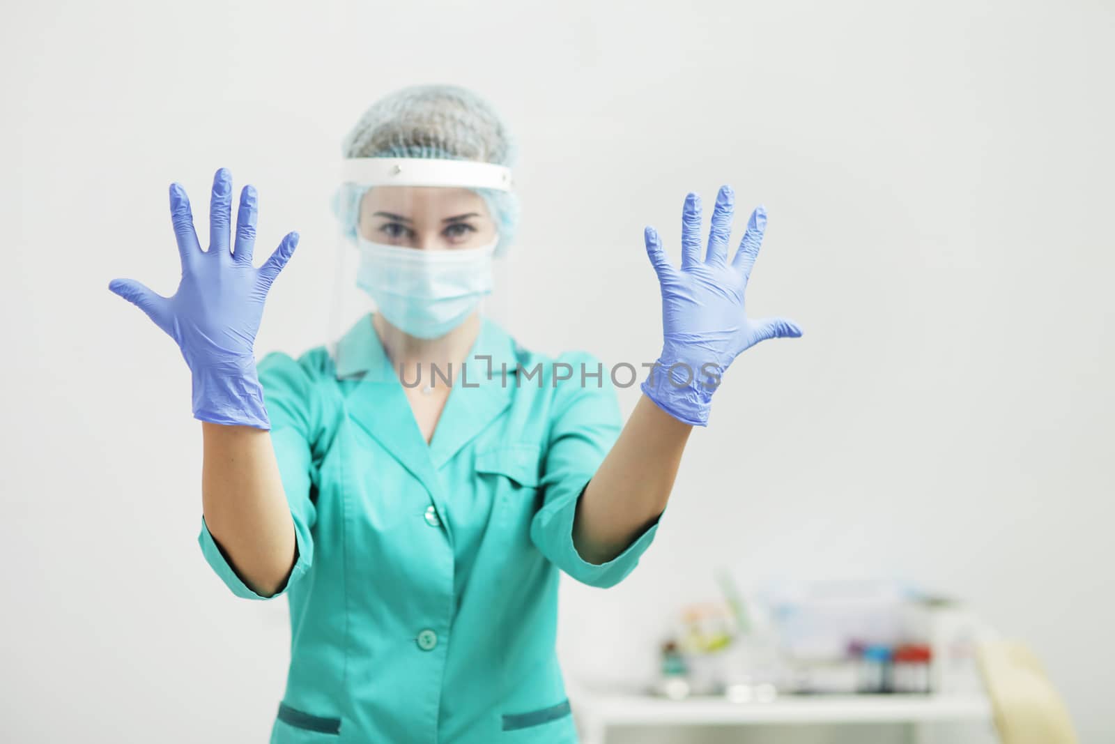 A woman doctor in uniform, medical mask, protective shield shows hands in gloves by selinsmo