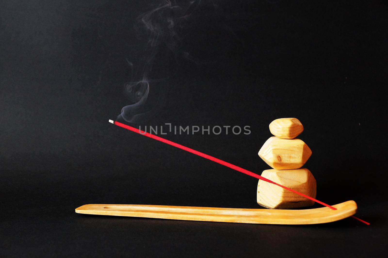 smoking incense stick on wooden stand and wooden tumi ishi on black background.