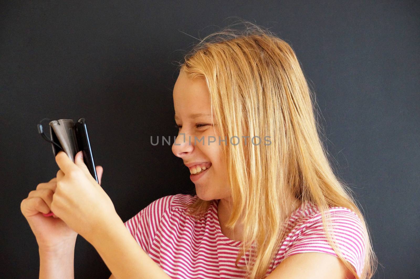 portrait of laughing teenage girl with phone on black background by Annado