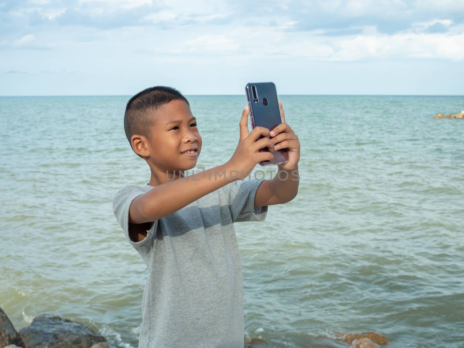 A boy using a phone to take a selfie on a sea background