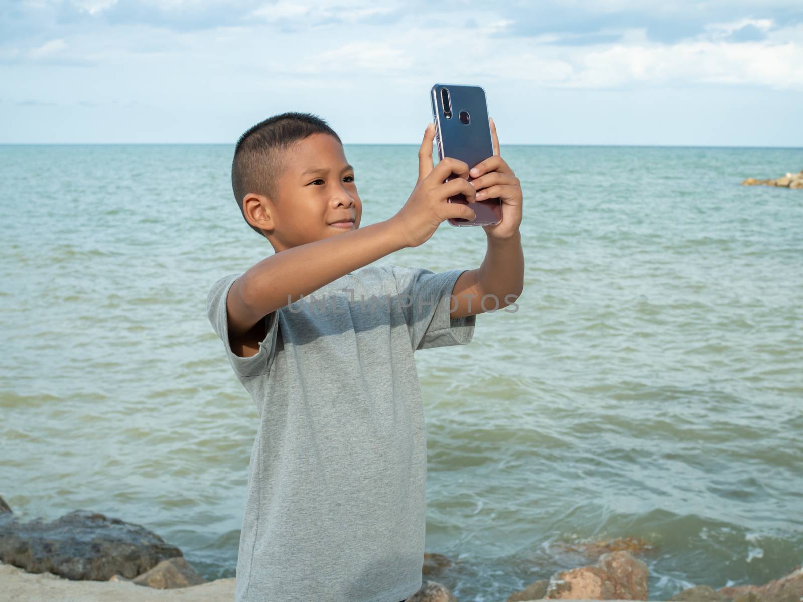 A boy using a phone to take a selfie on a sea background by Unimages2527