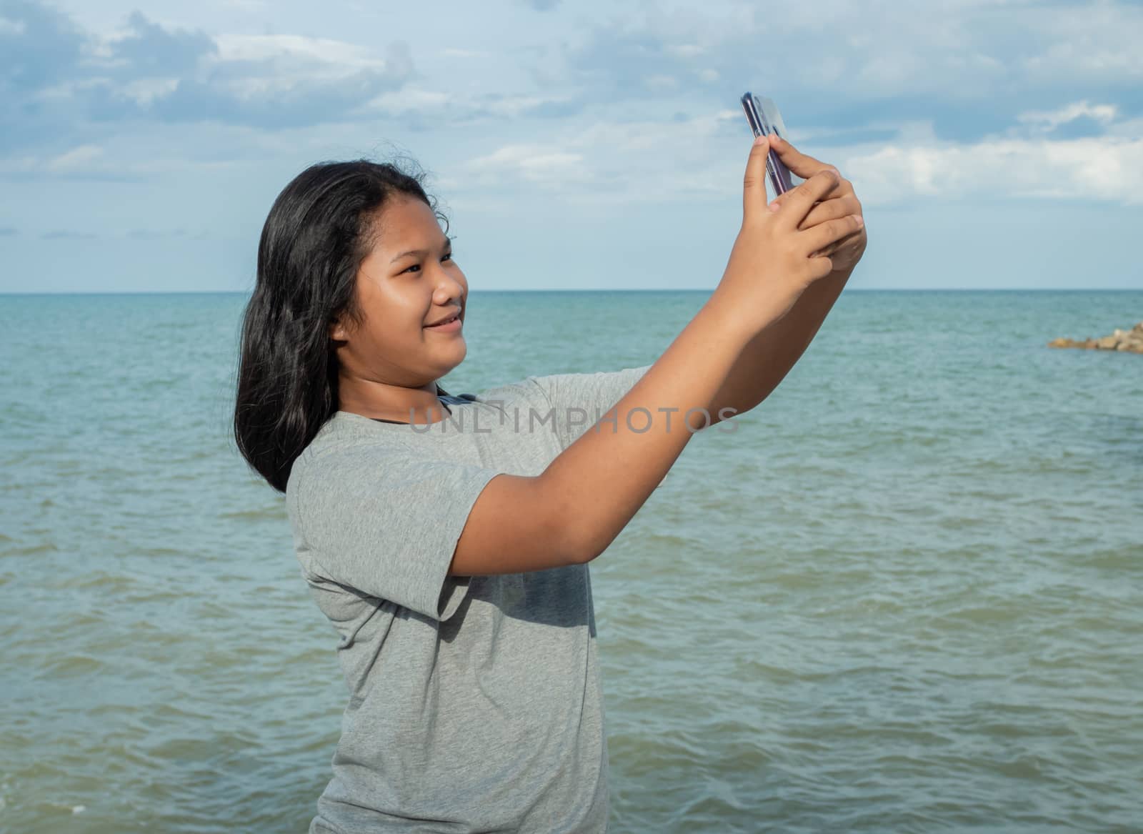 A girl using a phone to take a selfie on a sea background by Unimages2527