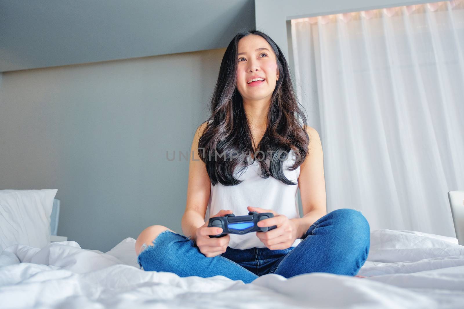Beautiful girl playing video game on bed by Surasak