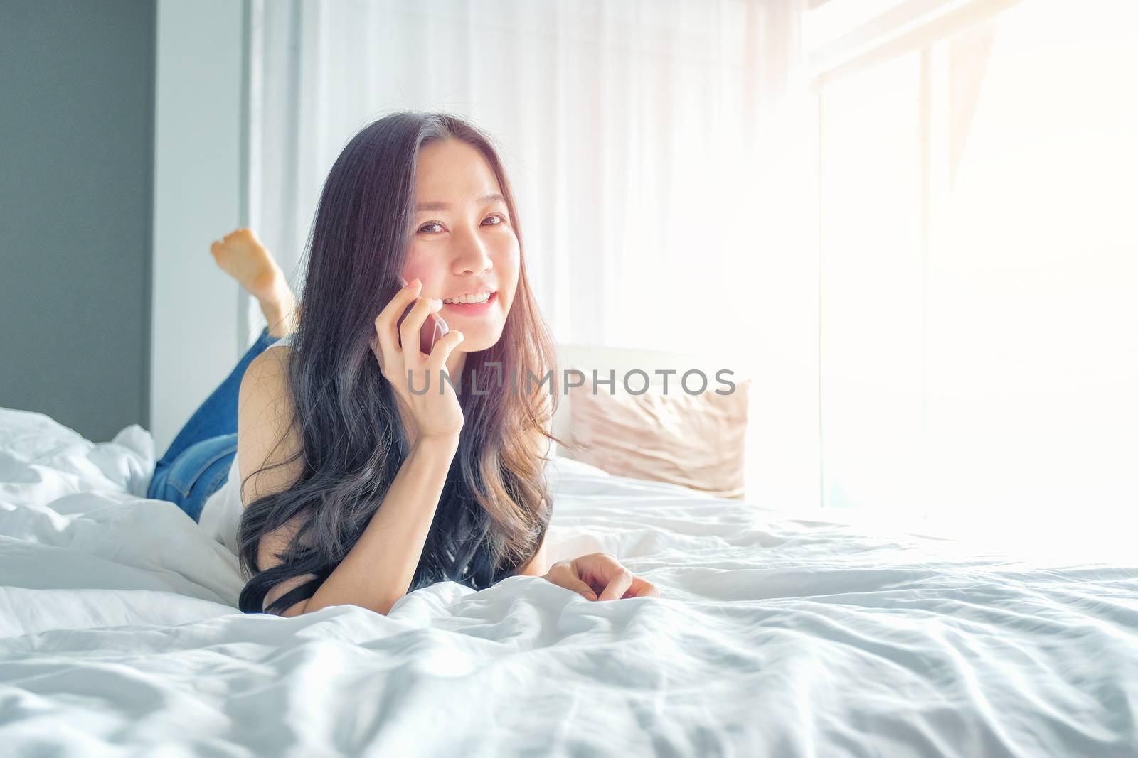 Young woman talking on the phone in bedroom at morning  by Surasak
