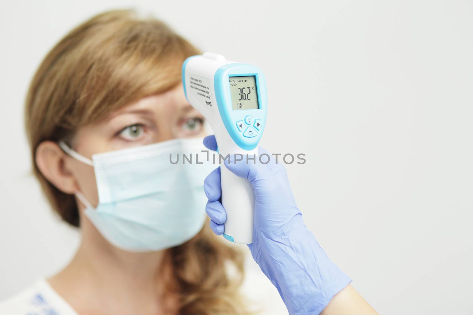 Medical woman in uniform, a medical mask, a face shield, and gloves measures the temperature of a woman with a pyrometer. A female doctor or nurse. Coronavirus COVID-19.