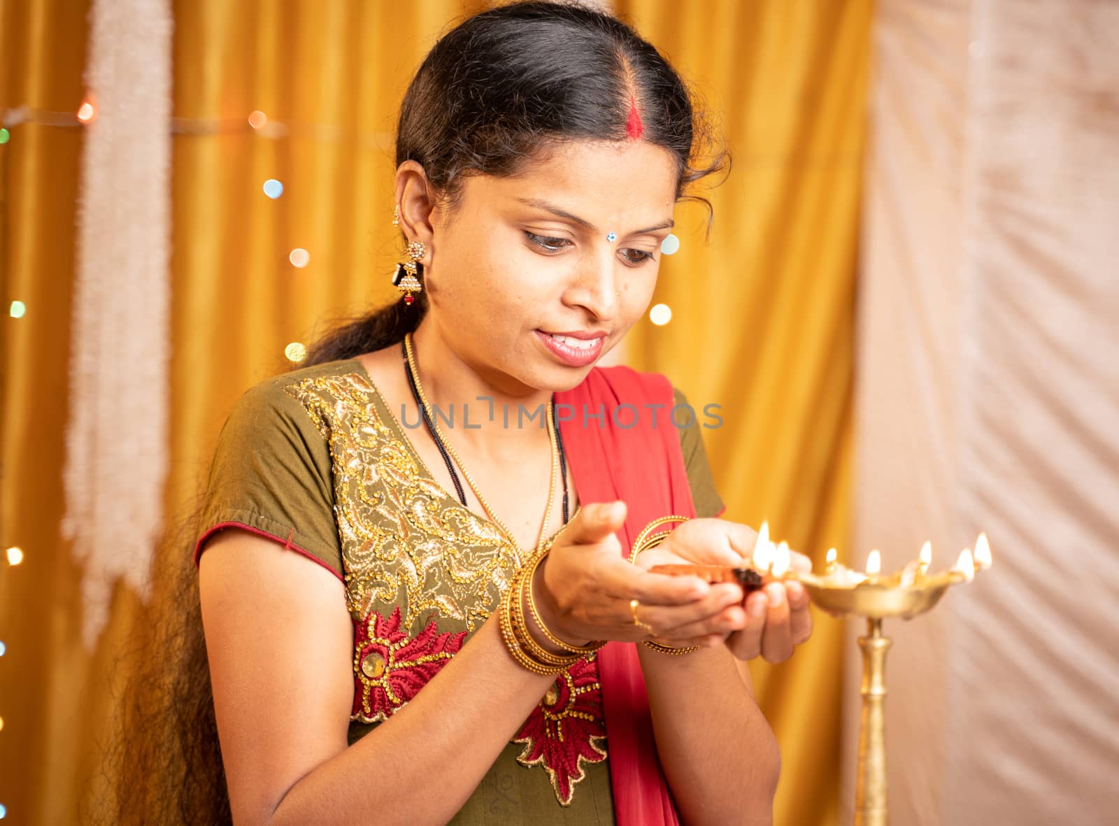 Happy smiling Indian woman lighting lantern or Diya Lamp during festival ceremony at home - concept of traditional festival and ritual celebrations. by lakshmiprasad.maski@gmai.com