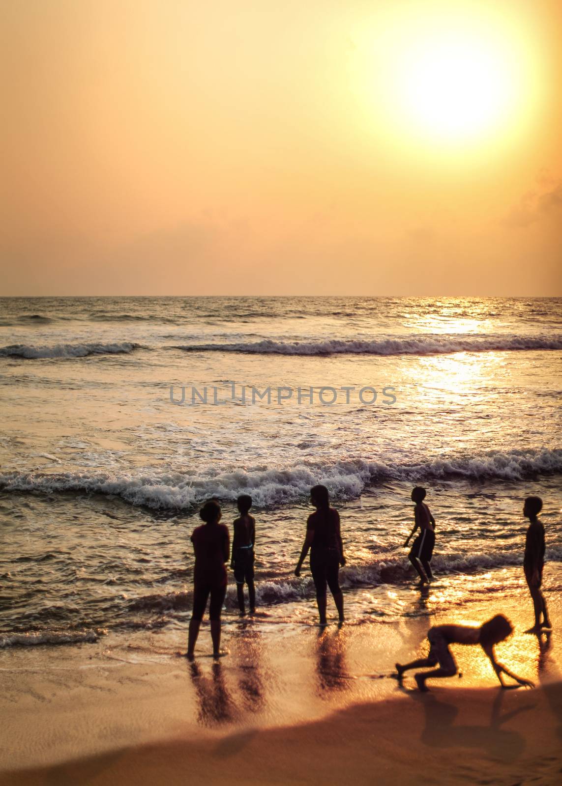 Kalutara, Sri Lanka - April 15, 2017: Silhouettes of people, mostly children playing on the beach in golden sunset evening light.