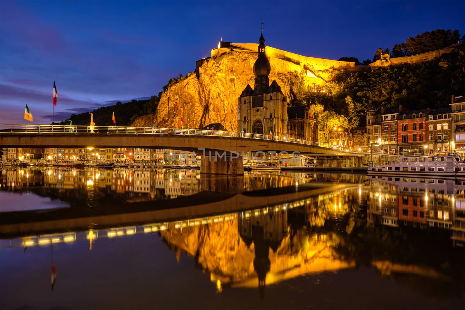 Night view of Dinant town, Collegiate Church of Notre Dame de Dinant over River Meuse and Pont Charles de Gaulle bridge and Dinant Citadel illuminated in the evening. Dinant, Belgium