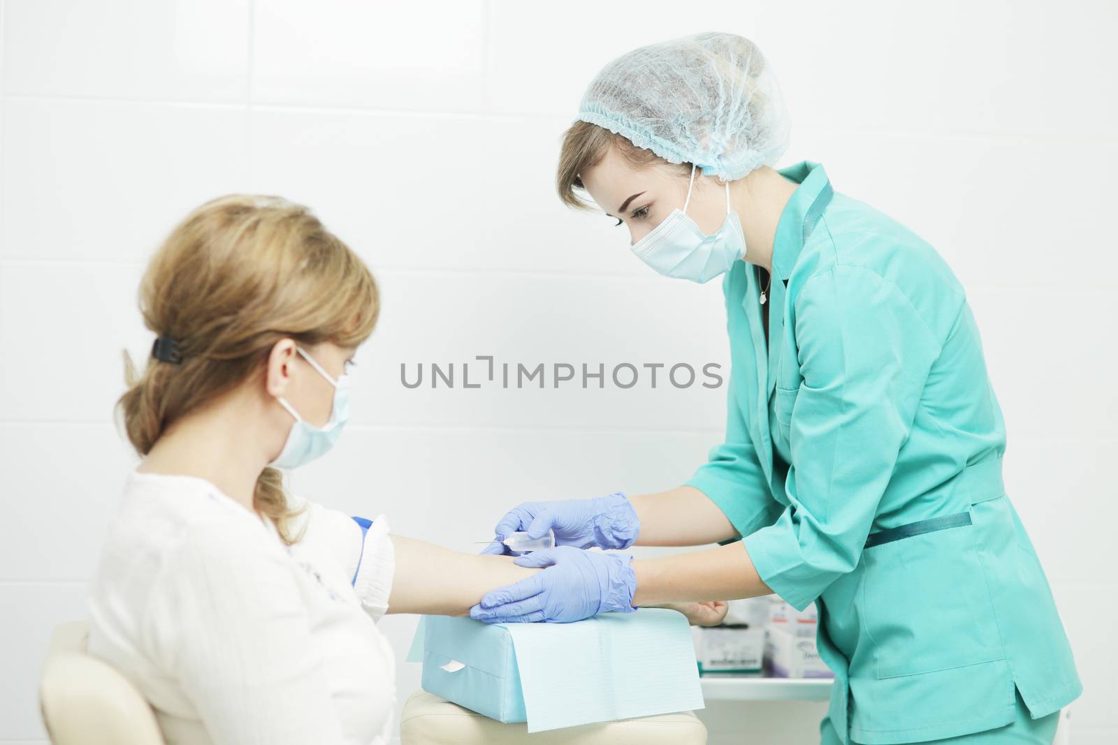 A female nurse in a medical mask takes a blood sample from the patient.