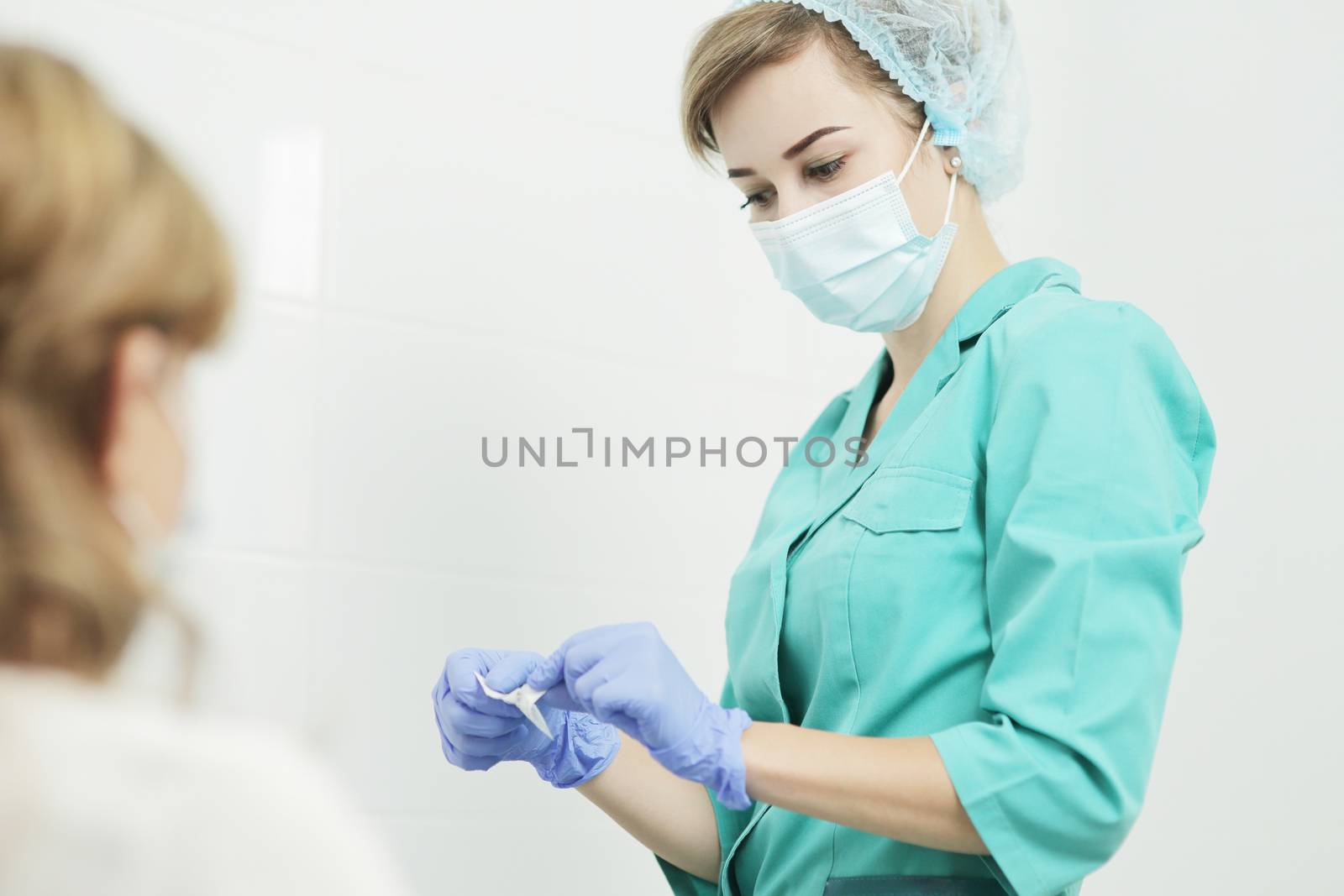 A nurse wearing a medical mask opens a disposable alcohol wipe. by selinsmo
