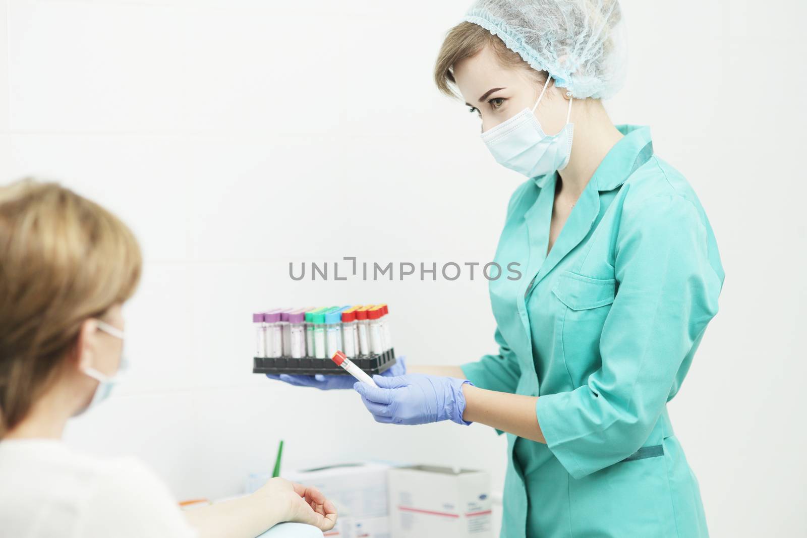 A female nurse in a medical mask holds a test tubes for a blood test by selinsmo
