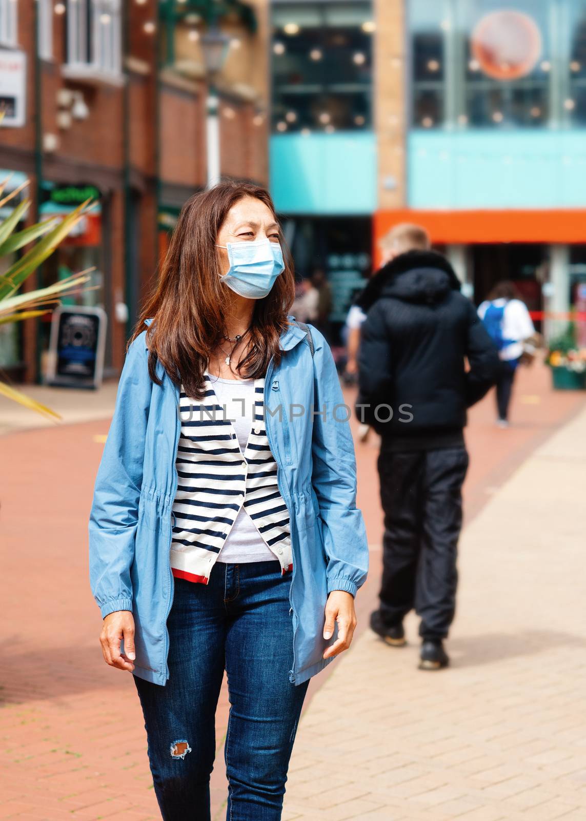 Asian woman in a face mask and a blue coat walking around Europe city