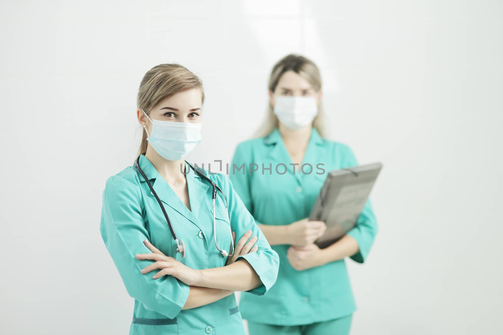 Two female doctors in medical masks looking at the camera. Stethoscope on neck by selinsmo