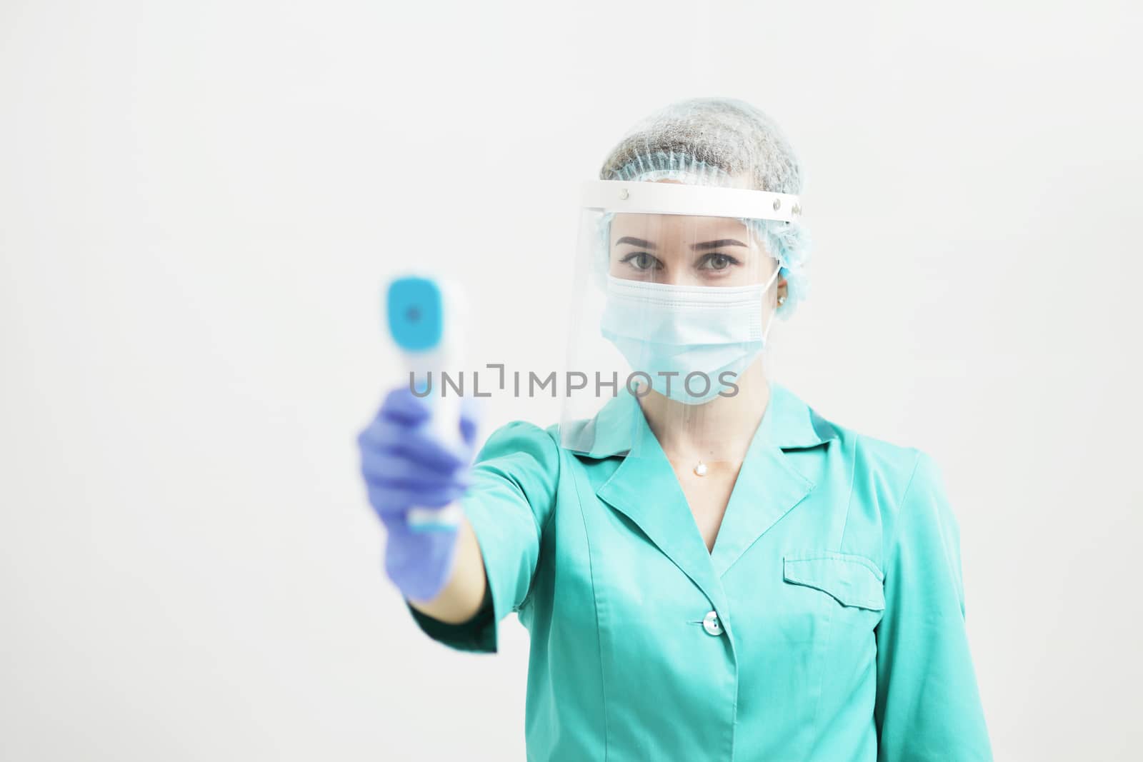 Female doctor or nurse in protective mask at hospital holds pyrometer in hand. Safety measures against the coronavirus. Prevention Covid-19 healthcare concept. Stethoscope over the neck.