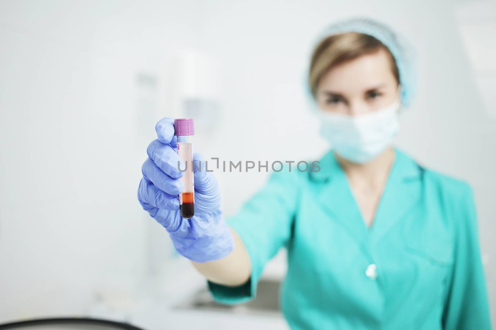 A female nurse in a medical mask holds a test tubes for a blood test by selinsmo