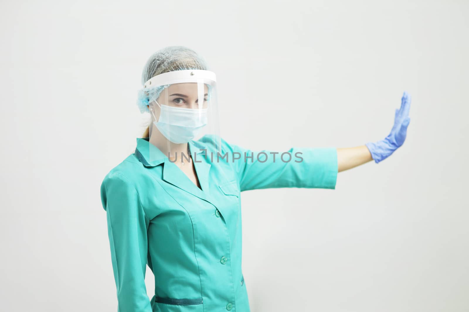 A woman doctor in uniform, medical mask, protective shield, gloves. Stop gesture by selinsmo