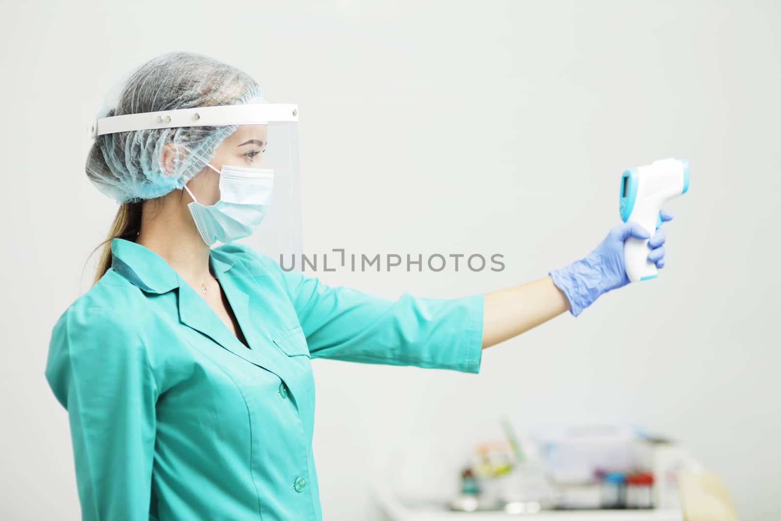 Female doctor or nurse in protective mask at hospital holds pyrometer in hand. Safety measures against the coronavirus. Prevention Covid-19 healthcare concept. Stethoscope over the neck.
