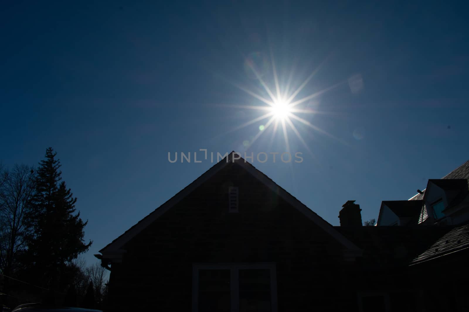 A Bright Sun Over a Silhouetted Suburban Building and Trees