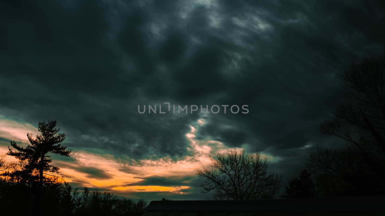 A Stormy Sunset With Silhouette Trees in the bottom of the frame by bju12290