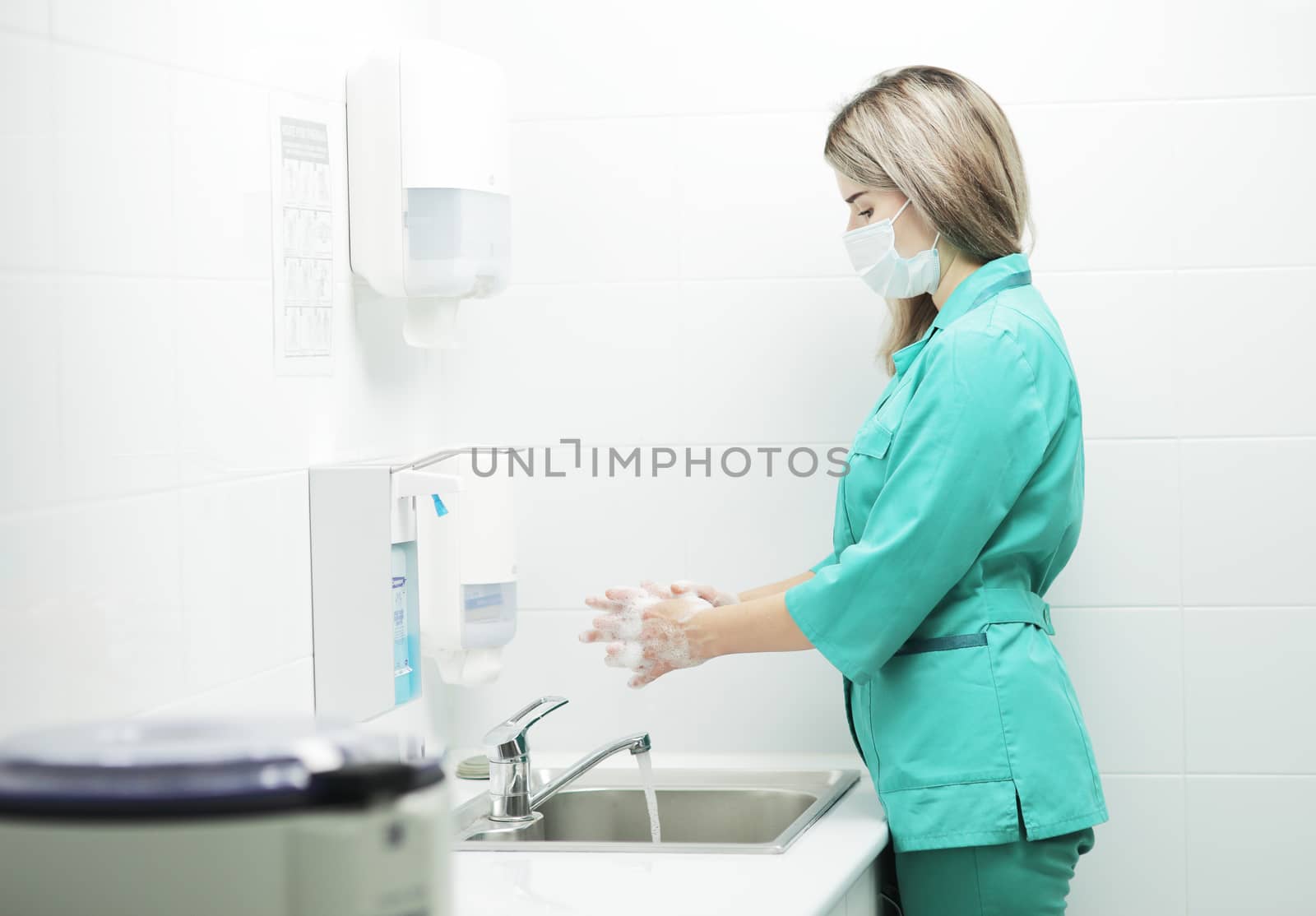 A woman doctor in protective mask washes hands thoroughly in hospital by selinsmo