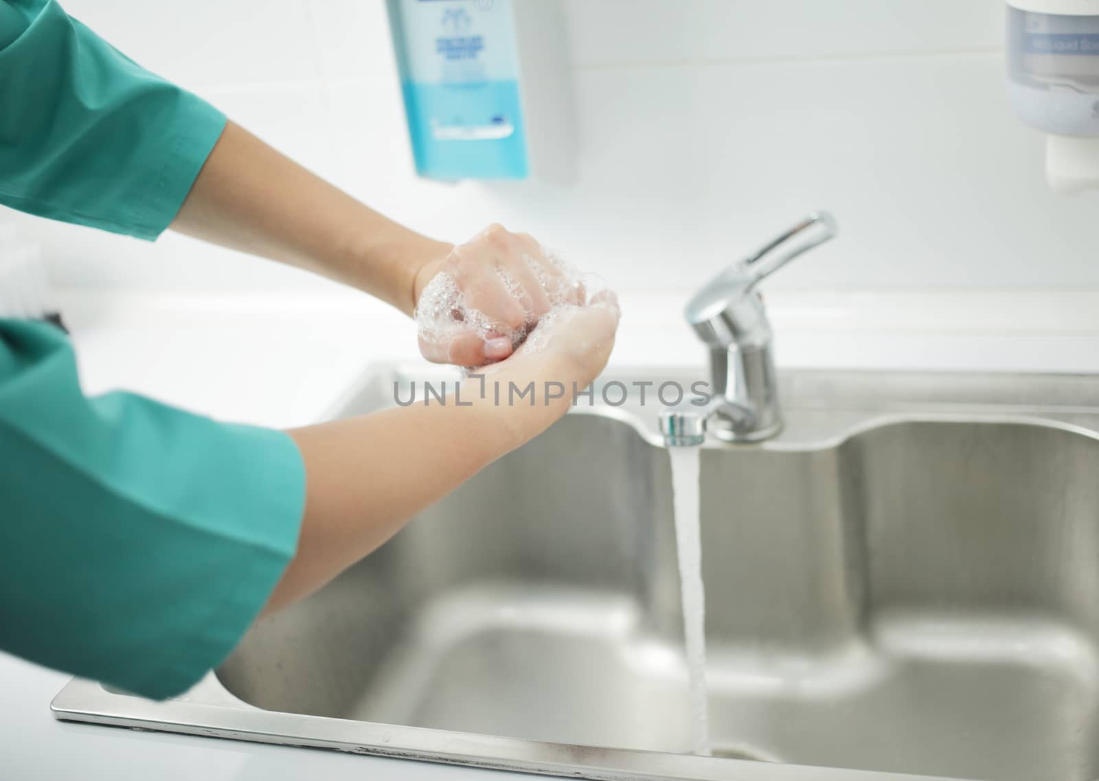 A woman doctor in a protective mask and medical uniform washes her hands thoroughly in the hospital. Soaped hands in foam