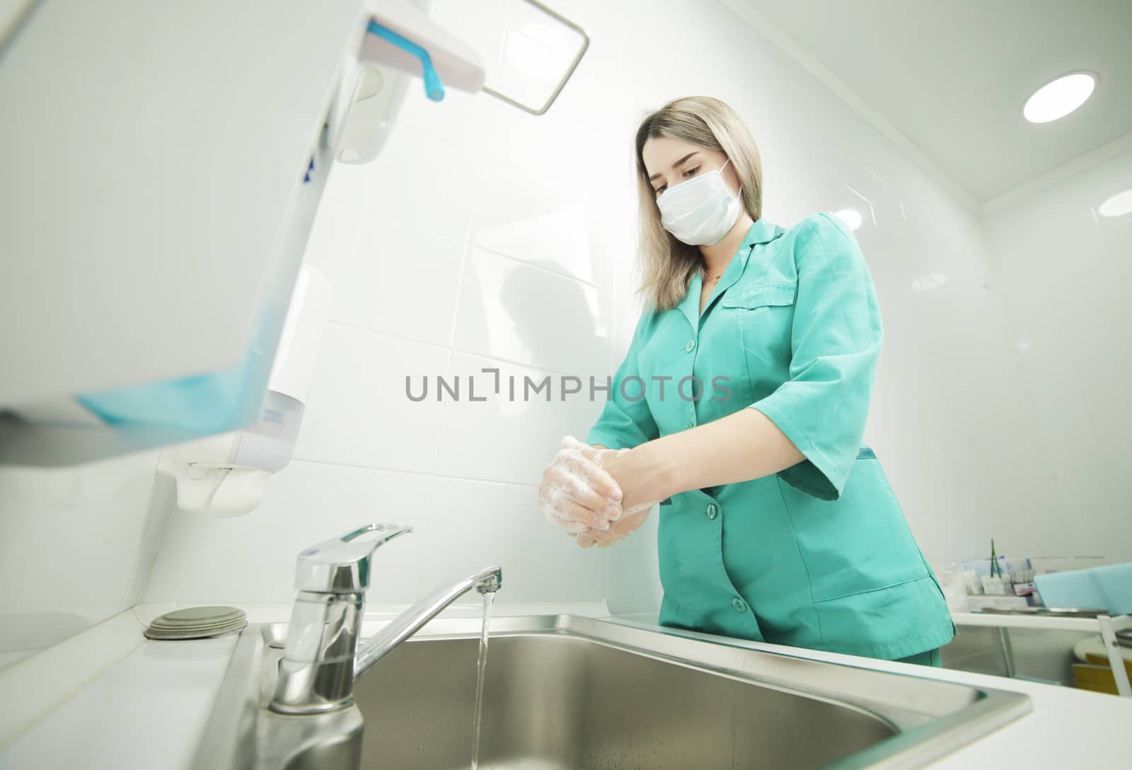 A woman doctor in protective mask washes hands thoroughly in hospital by selinsmo