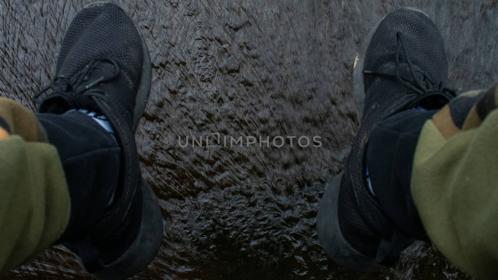 A Man's Feet in Black Running Shoes and Camo Pants Dangling Over Running Water
