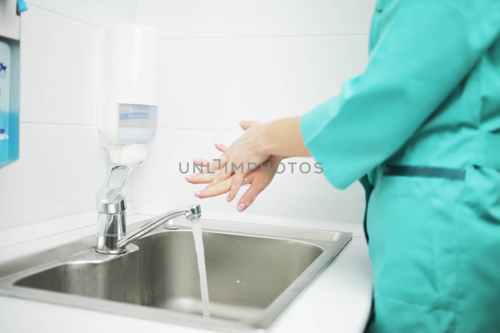 A woman doctor in a protective mask and medical uniform washes her hands thoroughly in the hospital. Soaped hands in foam
