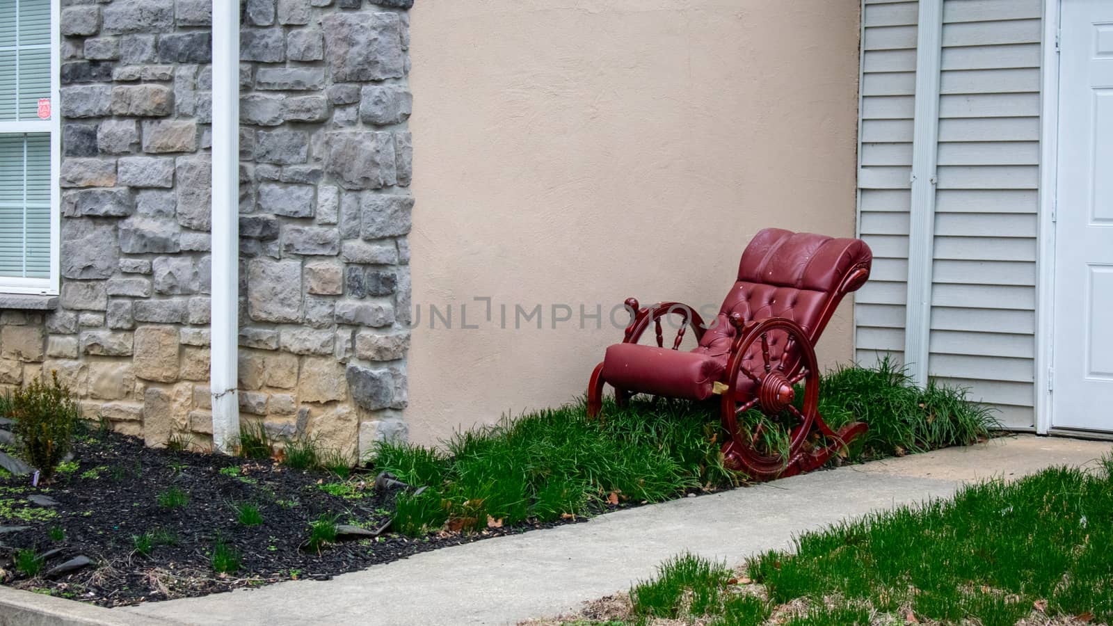 An Old-Fashioned Cushioned Red Rocking Chair Sitting in a Patch of Grass Next to a Building