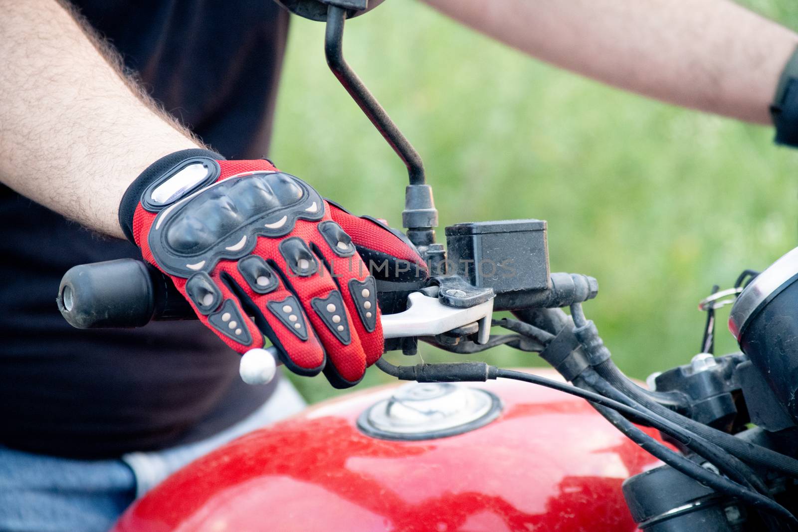 Young indian man wearing red riding gloves with protection while holding the handle bars of a motorcycle with a red tank by Shalinimathur