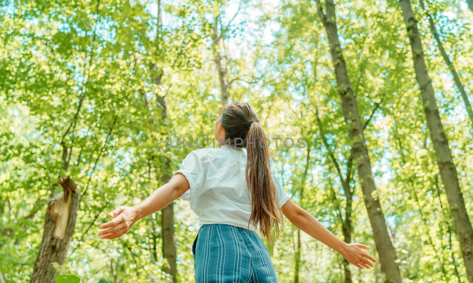 Free woman breathing clean air in nature forest. Happy girl from the back with open arms in happiness. Fresh outdoor woods, wellness healthy lifestyle concept by Maridav