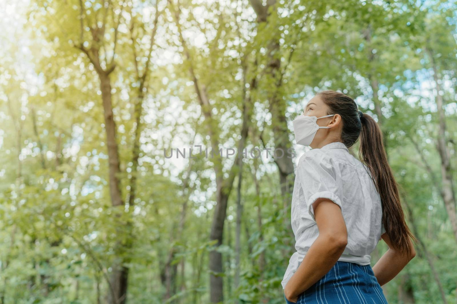 Eco-friendly sustainable face mask. Woman wearing kn95 korean masks walking in outdoor forest lookin up at sunlight. Hope concept for environment. Coronavirus covering.