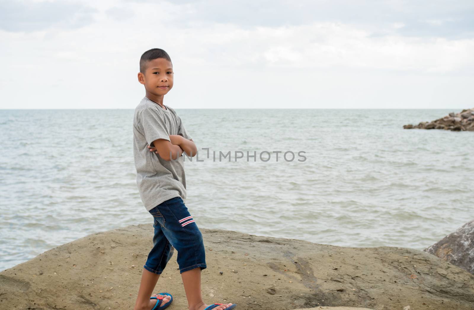 Portrait of a boy standing on a rock with a sea background.