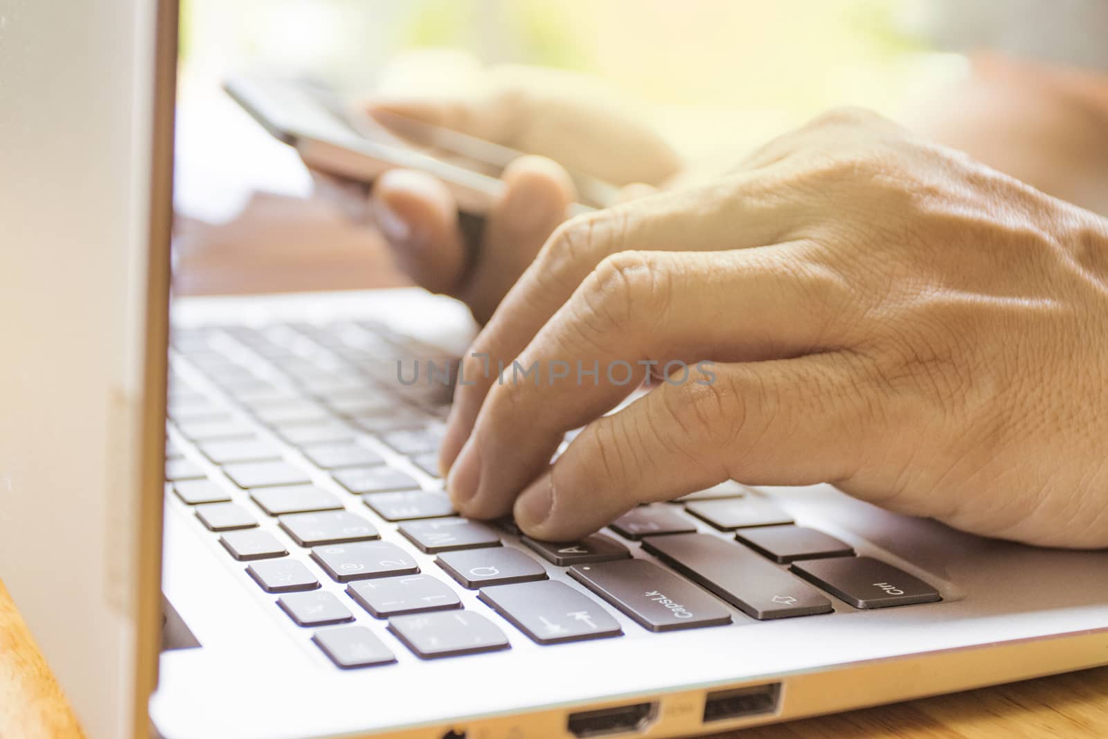  man is typing on a laptop with hand hold smart phone 