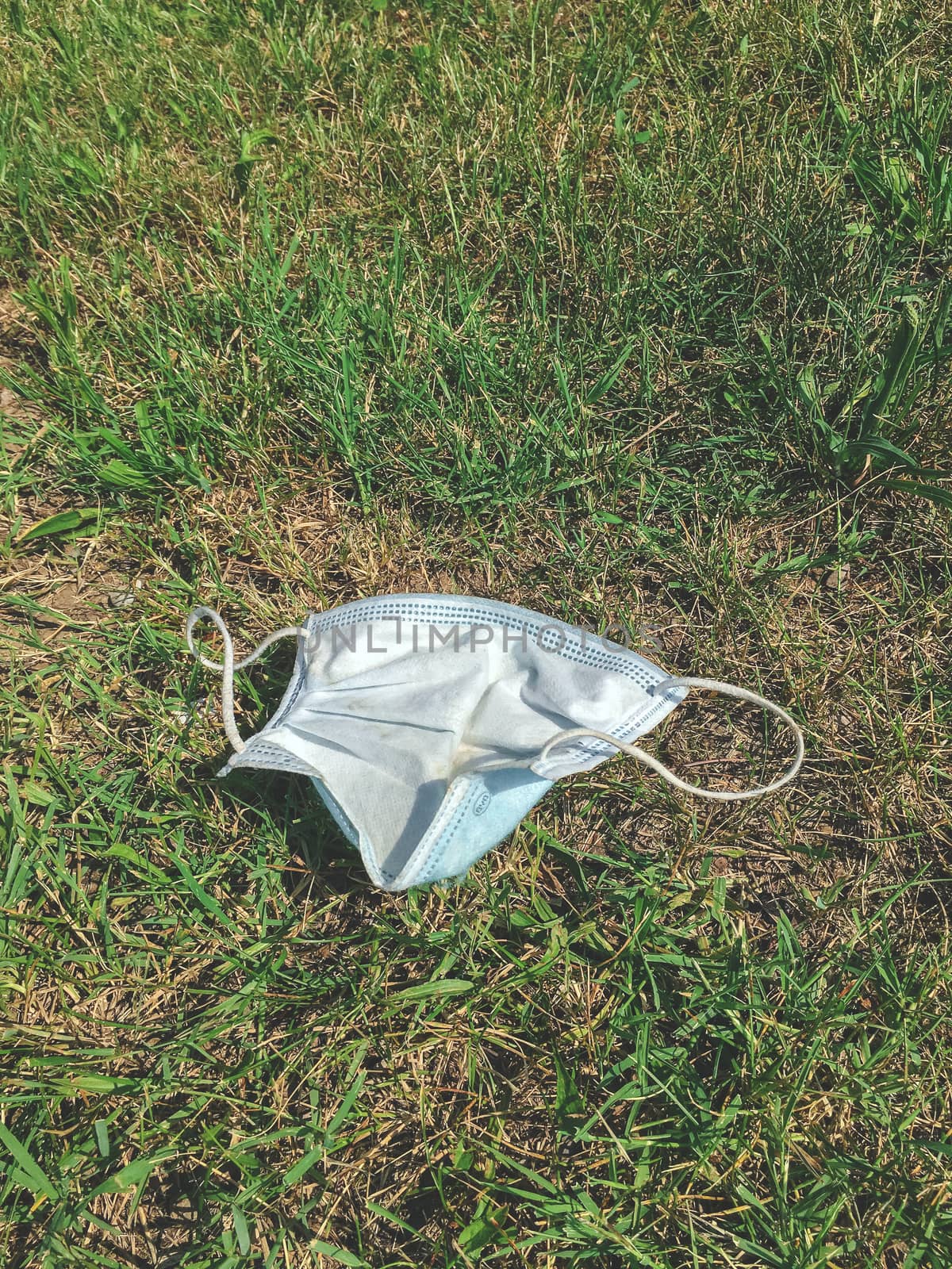 Disposable medical mask thrown on the street in the grass. The concept of environmental pollution after the coronavirus pandemic.