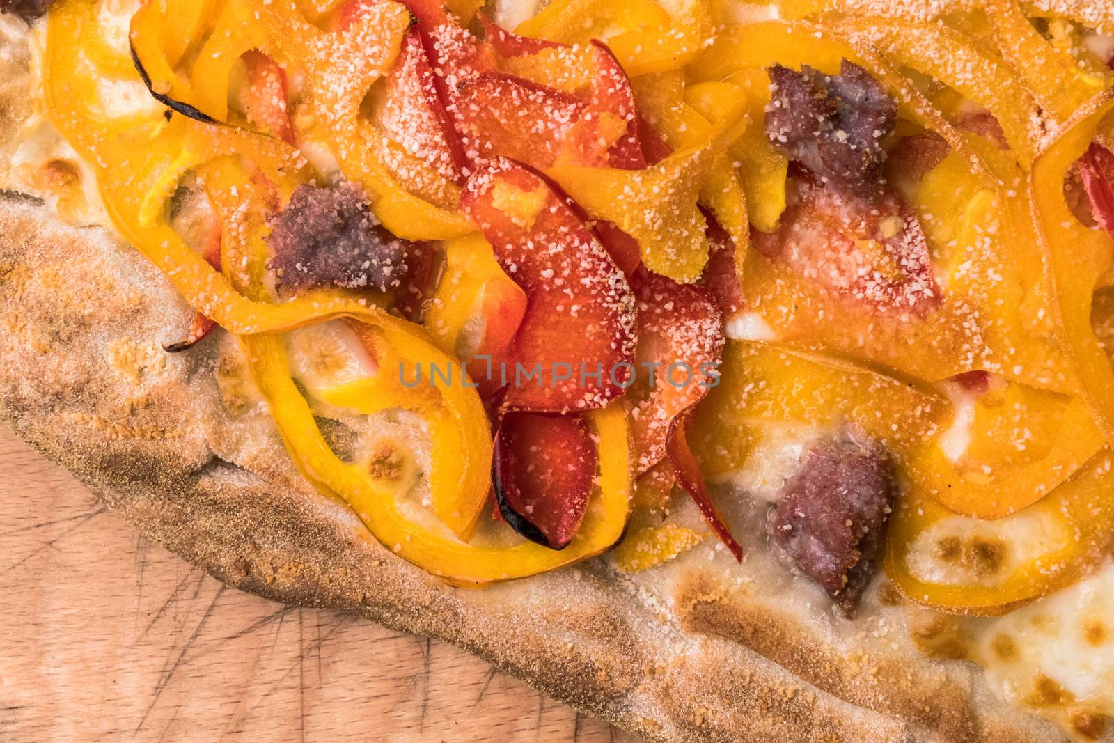 Pizza with bell peppers, sausages, mozzarella and parmesan cheese on rustic wooden background. Top view and close-up of piece.