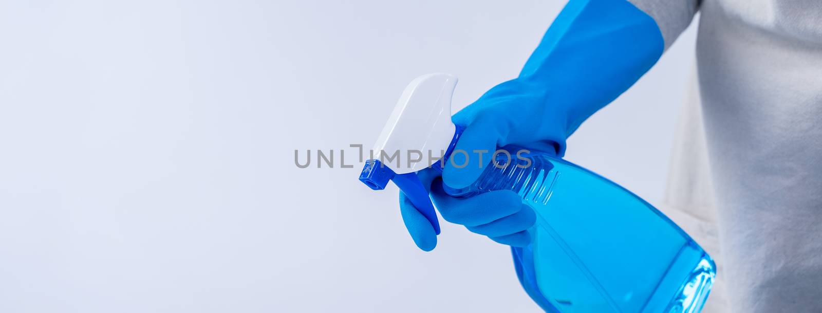 Young woman housekeeper in apron is cleaning, wiping down table surface with blue gloves, wet yellow rag, spraying bottle cleaner, closeup design concept.