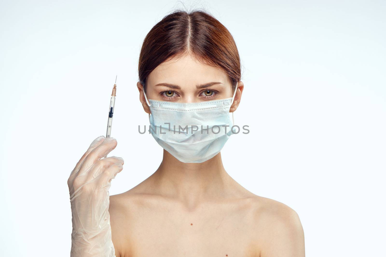 woman holding syringes in her hand injections medical mask naked shoulders rejuvenation light background. High quality photo