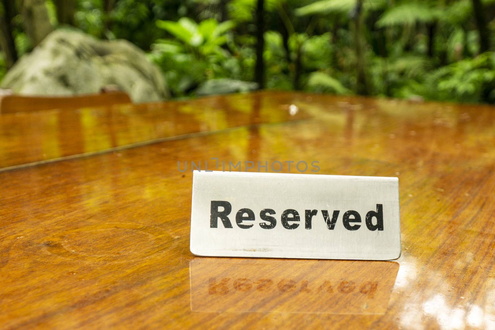 Reserved sign made out stainless steel plate on a laminated wooden table of a restaurant with trees and forest in the background. by sonandonures