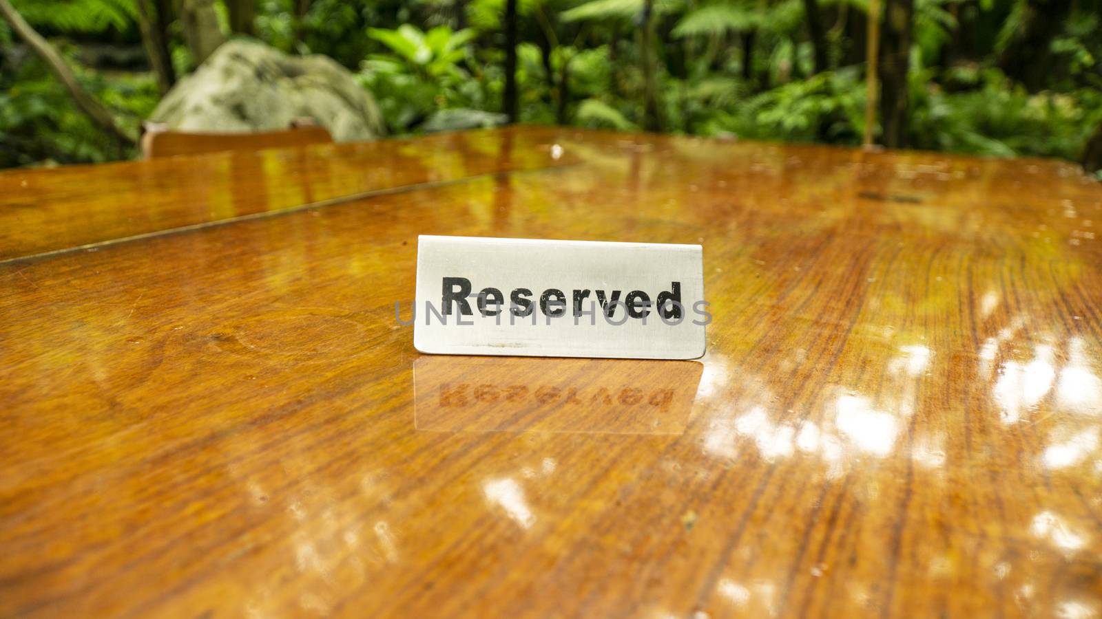 Reserved sign made out stainless steel plate on a laminated wooden table of a restaurant with trees and forest in the background.