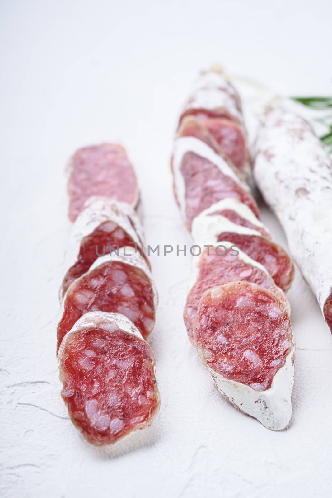 Variety of dry cured fuet and chorizosalami sausages, whole and sliced on white textured background.