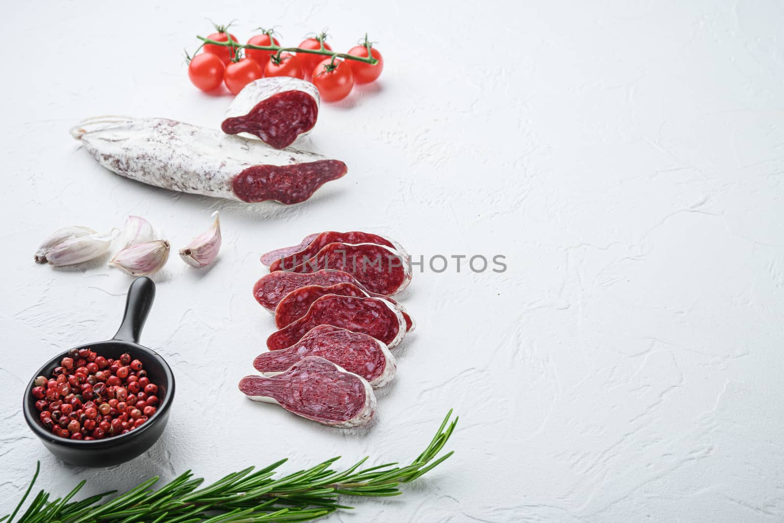 Sliced cuts of longaniza, dry cured spanish sausage with herbs and spices on white surface with copy space.