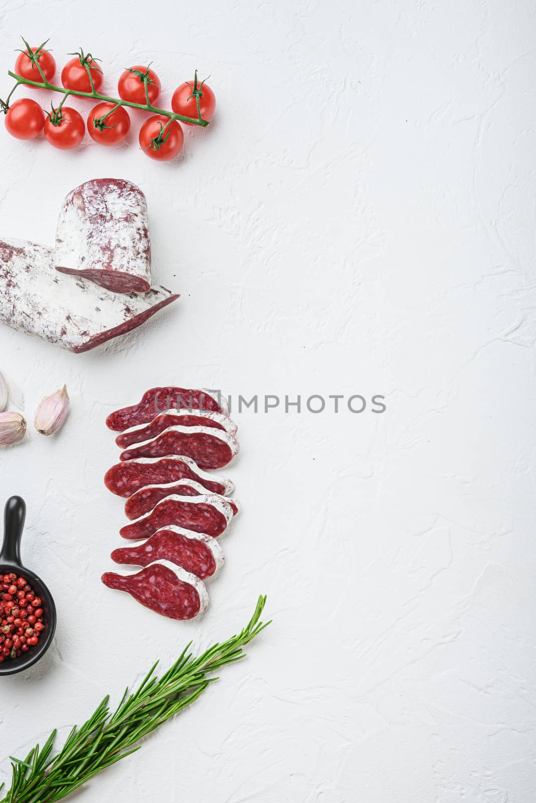 Sliced cuts of longaniza, dry cured spanish sausage with herbs and spices on white surface, top view with copy space.