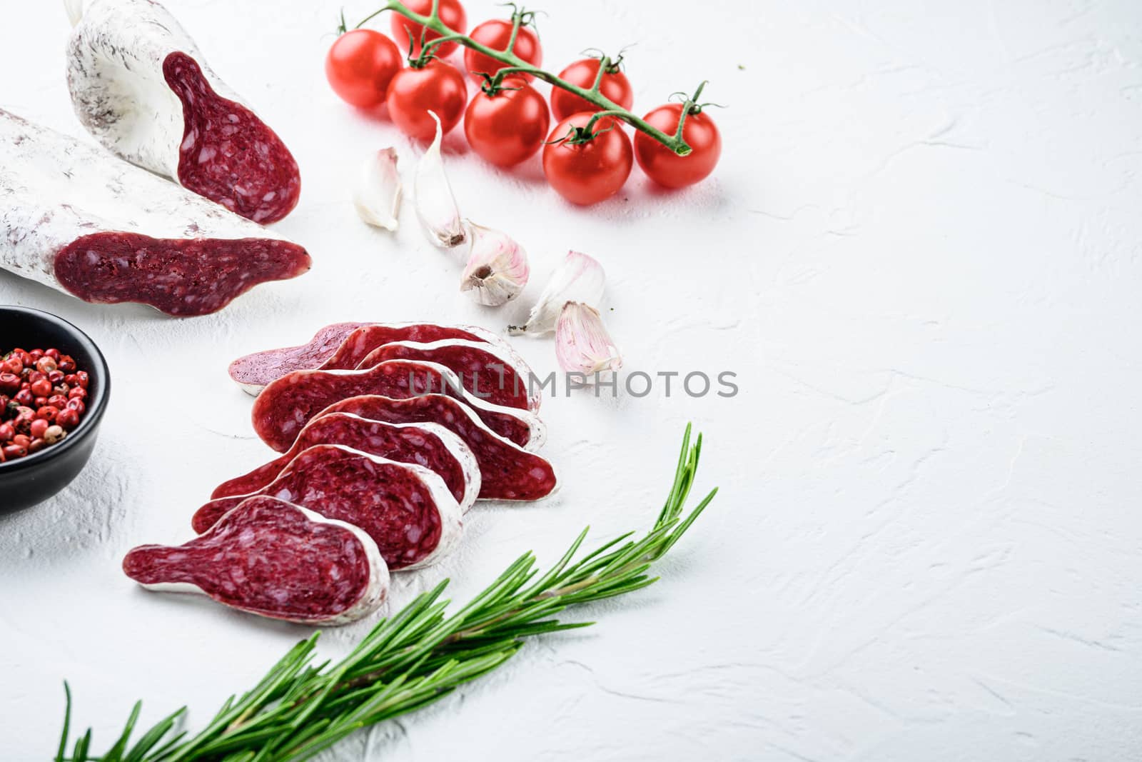 Sliced cuts of longaniza, dry cured spanish sausage with herbs and spices on white textured background with space for text.