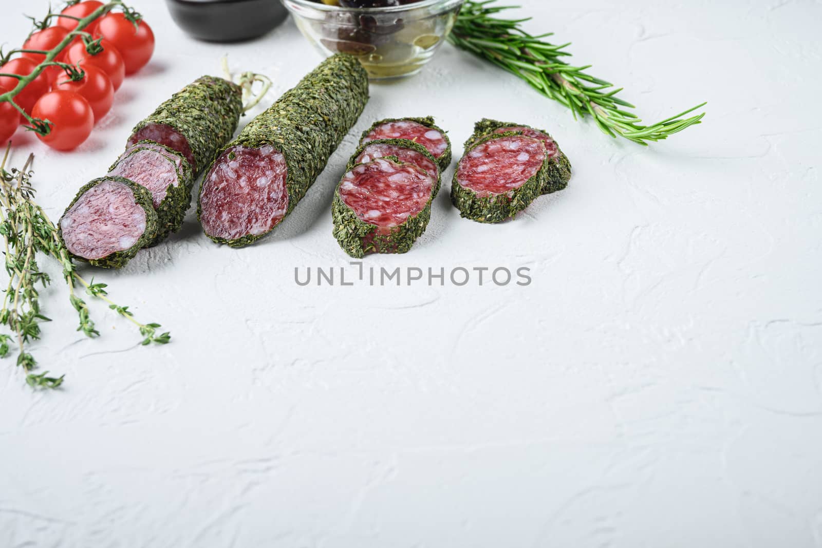 Traditianal fuet sausage in herbs with ingredients on white surface with copy space.